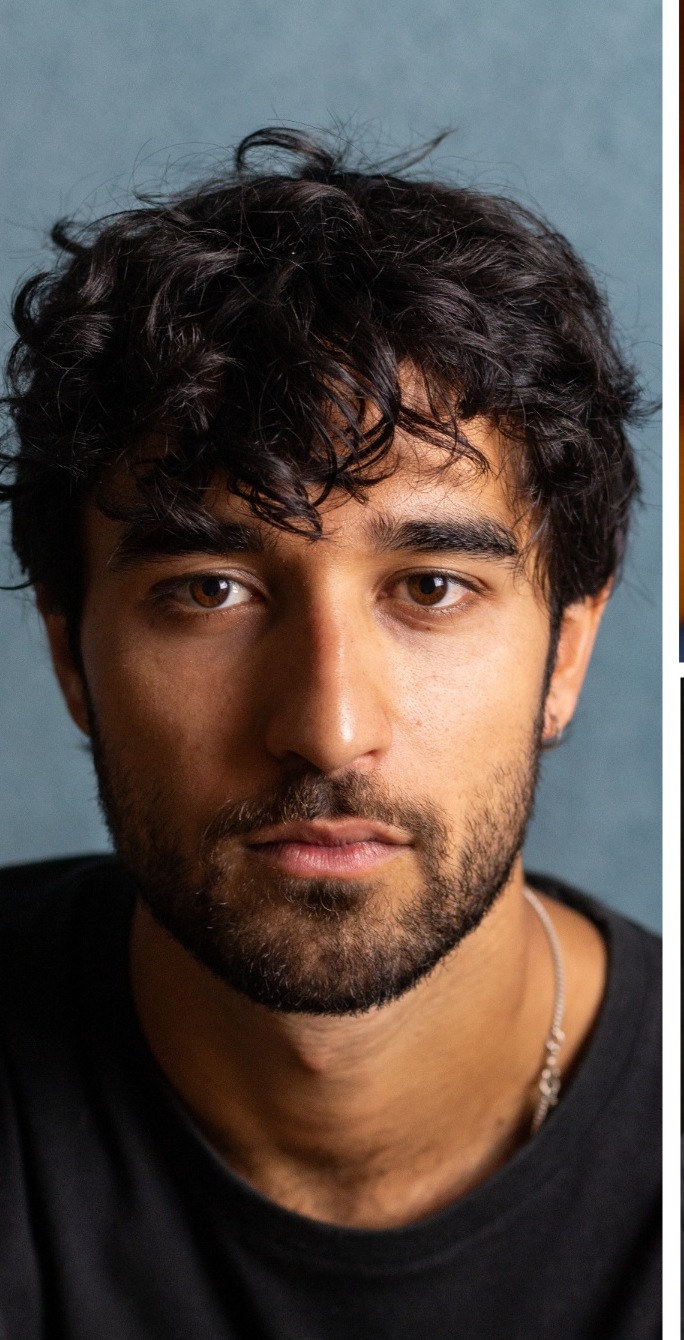 Adam Hashmi in a black shirt and silver chain, studio portrait against a blue-gray backdrop