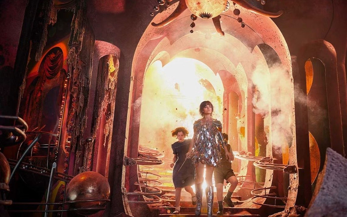 Emma Mackey as Jadis in a sequined dress leading Digory and Polly down a glowing arched stair in Narnia: The Magician’s Nephew